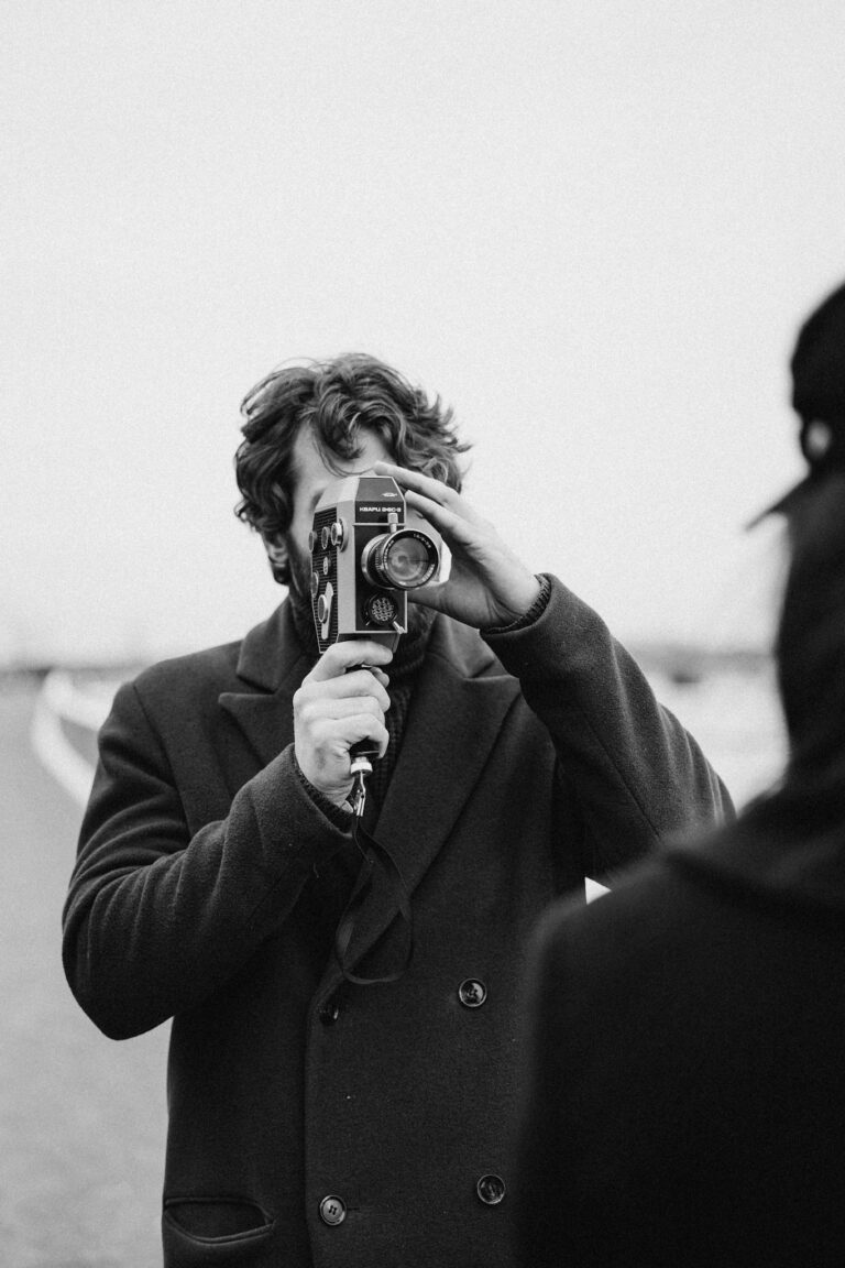 Monochrome image of a man with an old camera capturing a scene outdoors.